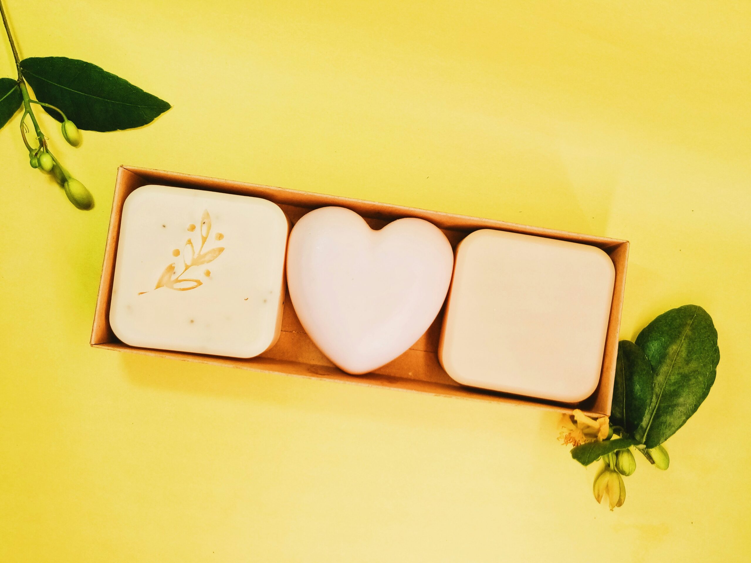 Gift box of three uniquely shaped natural soaps with heart and botanical designs on a bright yellow background
