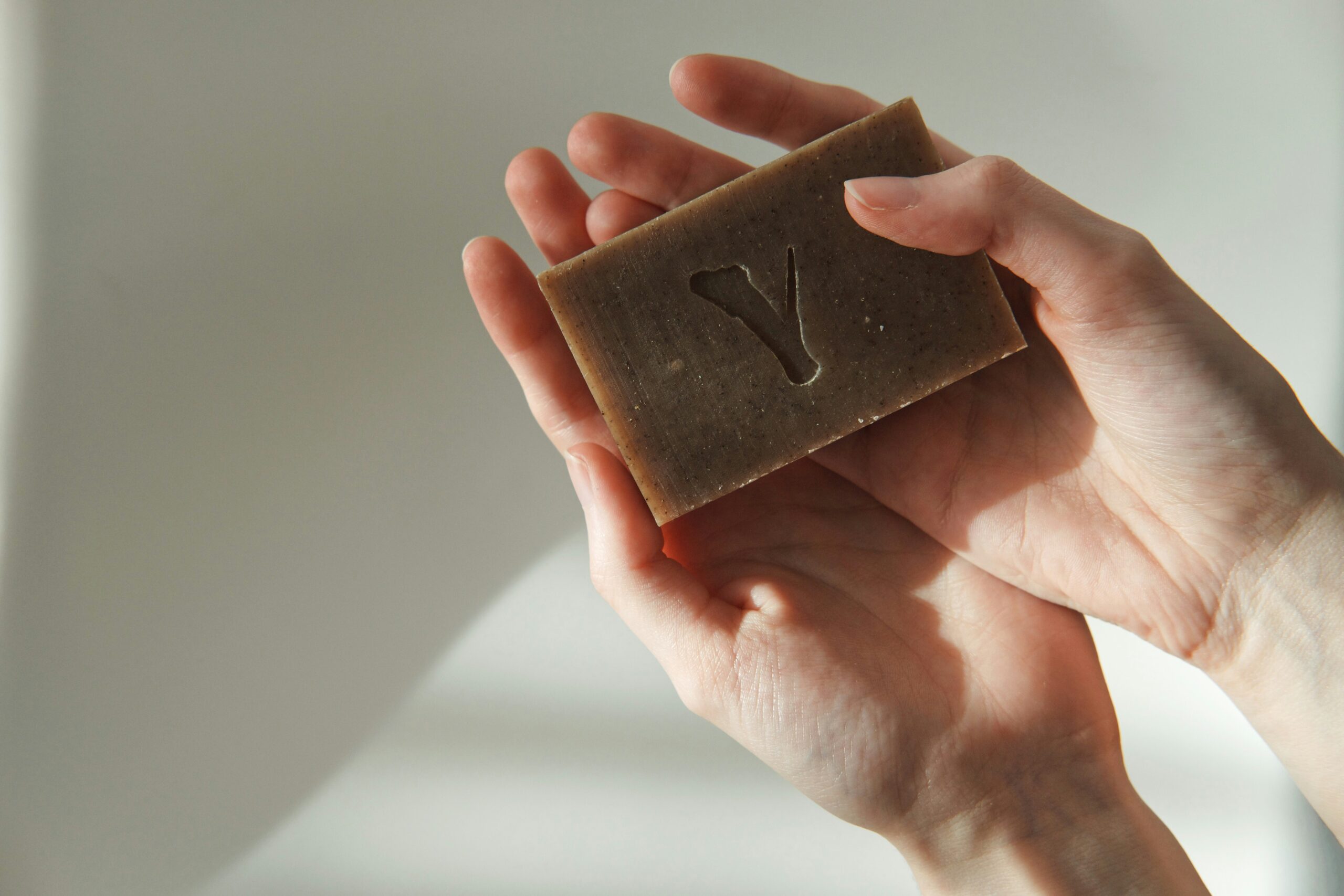 Hand holding a natural bar soap with embossed “V” logo, highlighting artisanal and private label craftsmanship